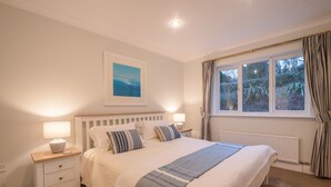 A bedroom with a large bed, bedside tables with lamps, a framed picture on the wall, and a window with curtains.