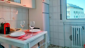 Een keuken met witte kasten, een raam met uitzicht op gebouwen, een radiator en een gedekte tafel met borden en glazen.