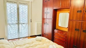 Een slaapkamer met een groot bed, een houten garderobe en een raam met gordijnen.