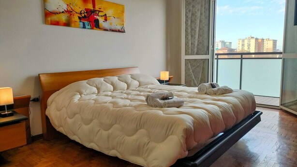 Een ruime slaapkamer met een groot bed, uitzicht op de stad vanaf een balkon en een schilderij aan de muur.