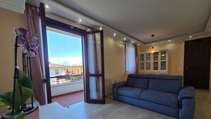 Un salón espacioso con un sofá azul, una planta en maceta y vistas al balcón exterior.