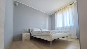 Un dormitorio con cama, mesita de noche y ventana con cortinas.