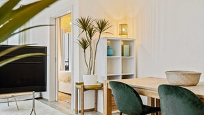 A modern living room with a TV, a dining table with chairs, a bookshelf, and a potted plant. - Chic Stay in Limpertsberg Near City Center (Luxembourg)