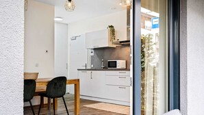 A modern kitchen with white cabinets, a microwave, and a wooden dining table with two chairs. - Chic Stay in Limpertsberg Near City Center (Luxembourg)