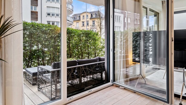 A modern apartment with a sliding glass door leading to a balcony with outdoor furniture. - Chic Stay in Limpertsberg Near City Center (Luxembourg)