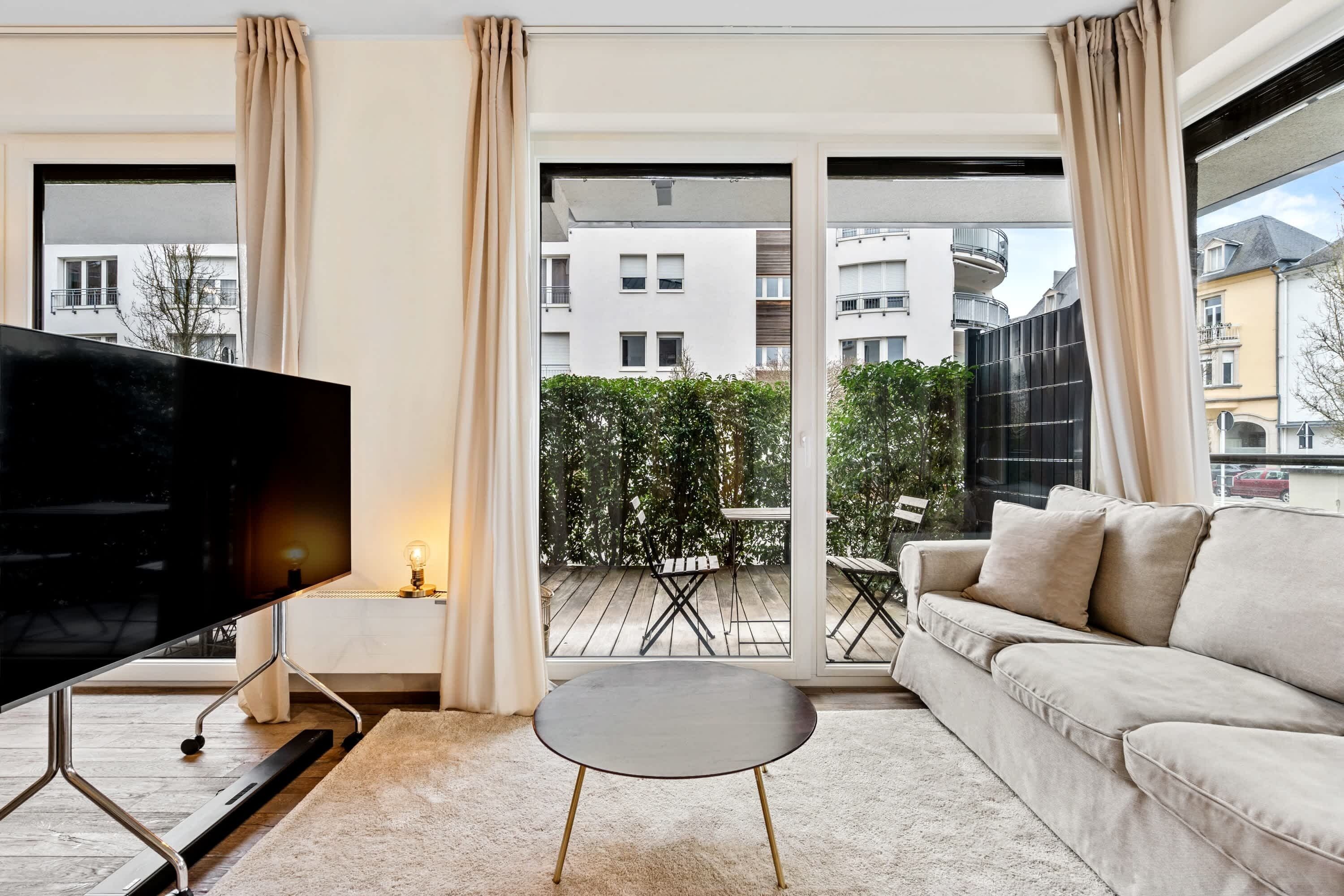 A modern living room with a flat-screen TV, a beige sofa, and a small round table.