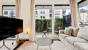 A modern living room with a flat-screen TV, a beige sofa, and a small round table.