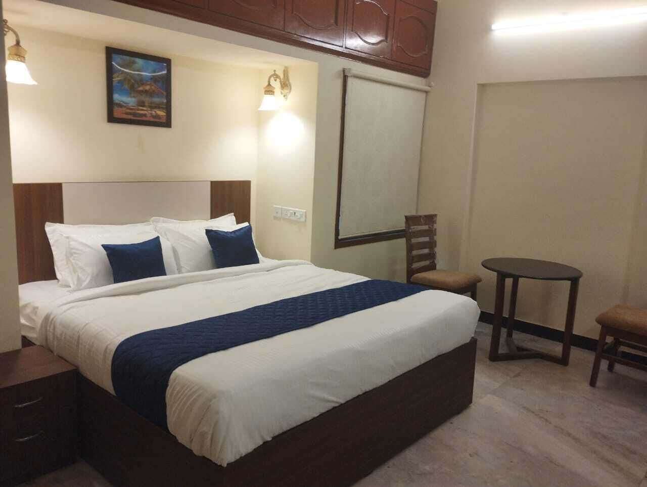 A hotel room with a large bed, two bedside tables, a small round table, and a chair.