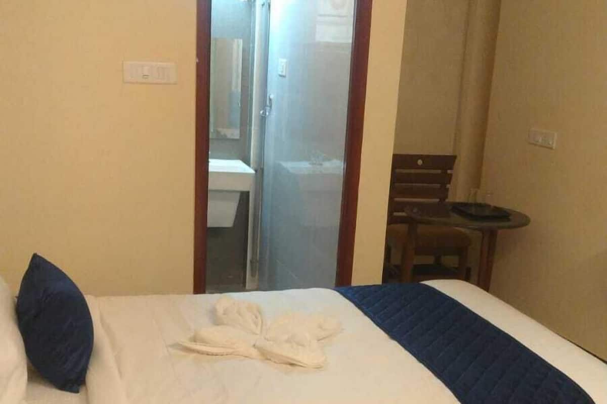 A hotel room with a bed, a small table, and an air conditioning unit.