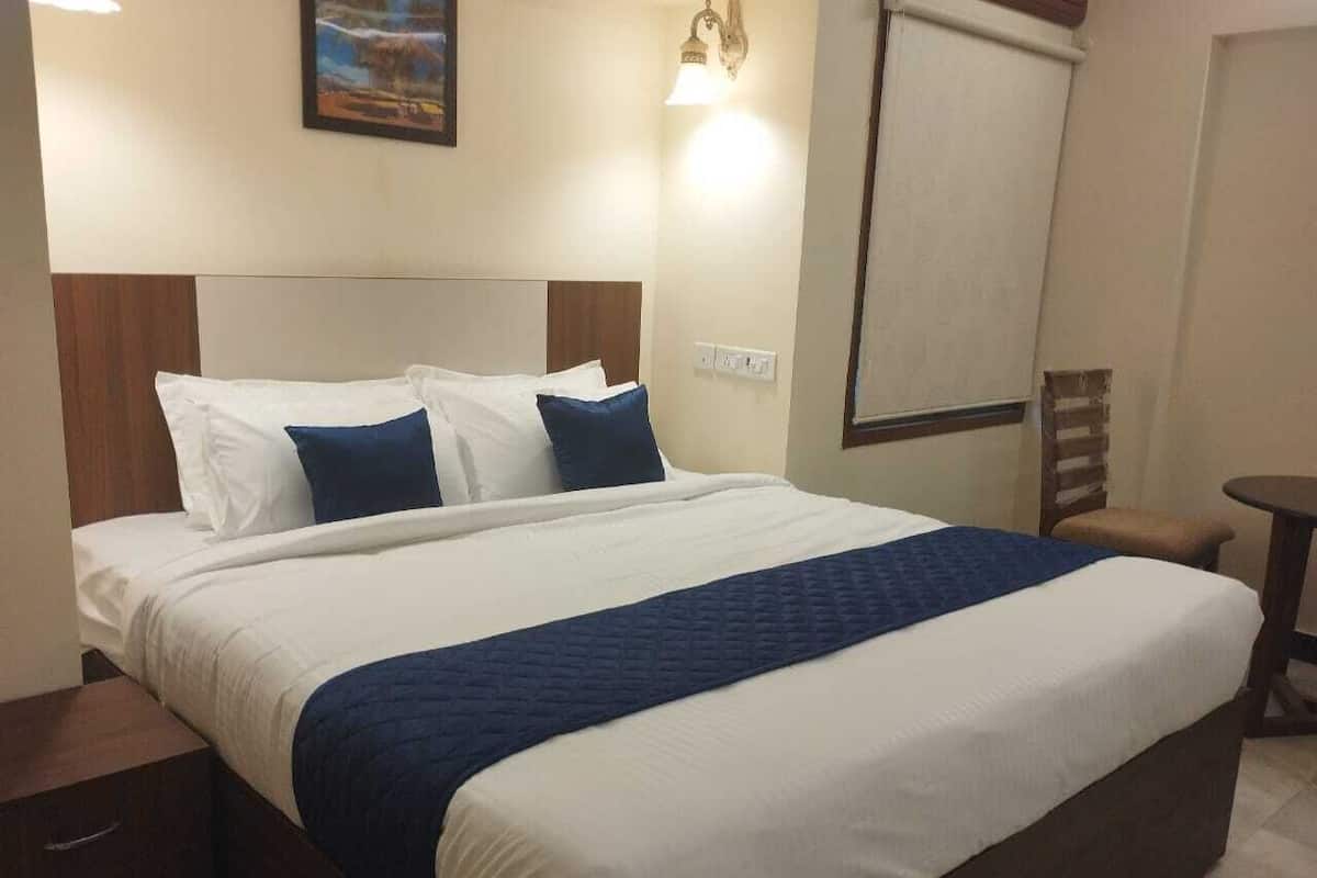 A hotel room with a large bed, a wooden headboard, a nightstand, a small table, and a wall-mounted light fixture.