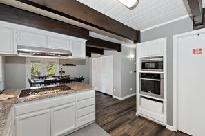 A modern kitchen with white cabinetry, a granite countertop, a stainless steel range hood, and built-in appliances including a microwave and oven.