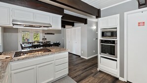 Une cuisine dotée de meubles blancs, d’un plan de travail en granit, d’une cuisinière en acier inoxydable et d’appareils électroménagers intégrés, notamment un four à micro-ondes et un four traditionnel.