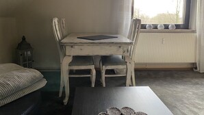 Un coin repas avec une table et des chaises blanches, une tablette noire posée sur la table et une fenêtre donnant sur des arbres.