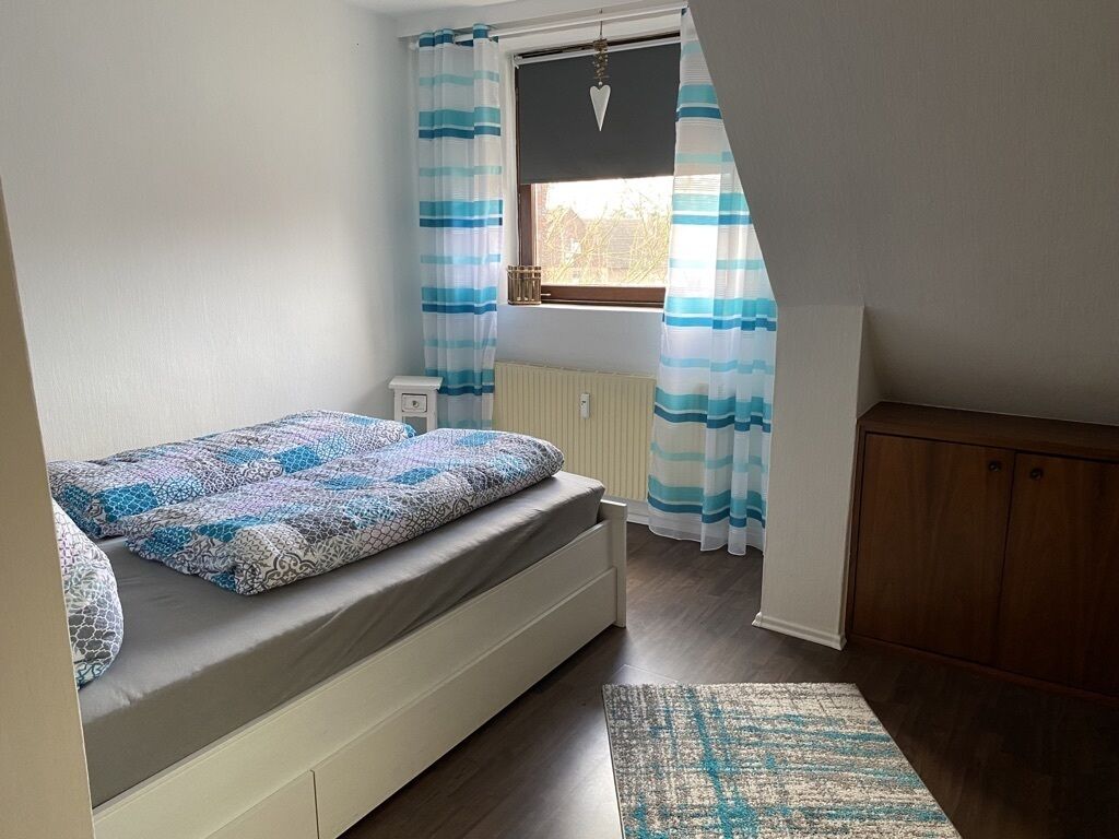 A bedroom with a bed, a radiator, a window with curtains, and a wooden cabinet.