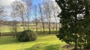Un champ verdoyant avec une clôture en bois, des arbres et un ciel dégagé.