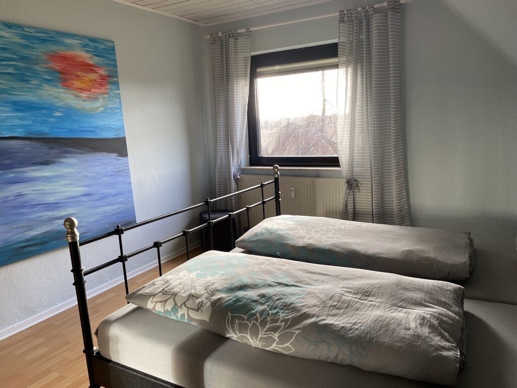 A bedroom with a bed, a window, and a painting on the wall.