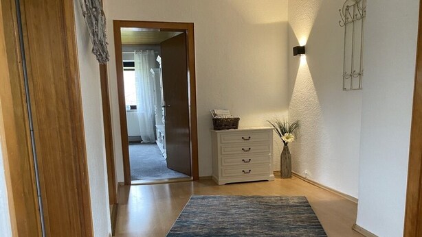 Un couloir avec un plancher en bois, un tapis bleu, une commode blanche et un luminaire fixé au mur.