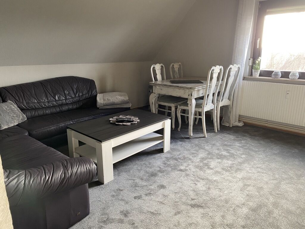A living room with a black leather sofa, a white coffee table, and a dining table with white chairs.