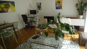 Een woonkamer met een bureau, stoelen, een open haard en kunstwerken aan de wanden.