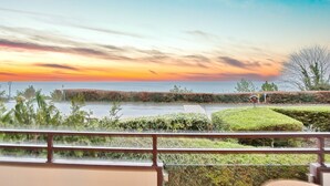 En balkon med udsigt over en anlagt have og havet i solnedgang.