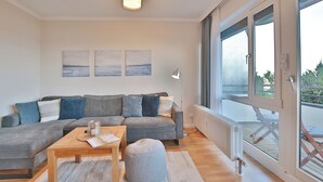 En moderne stue med en grå hjørnesofa, et træsofabord og en grå skammel. To abstrakte malerier hænger på væggen, og der står en gulvlampe.