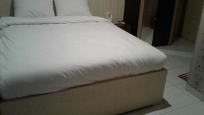 A neatly made bed in a hotel room with a headboard, a bedside table with a phone, and a door leading to another room. - OYO 93485 Hotel Kenzie Sentani (Sentani)