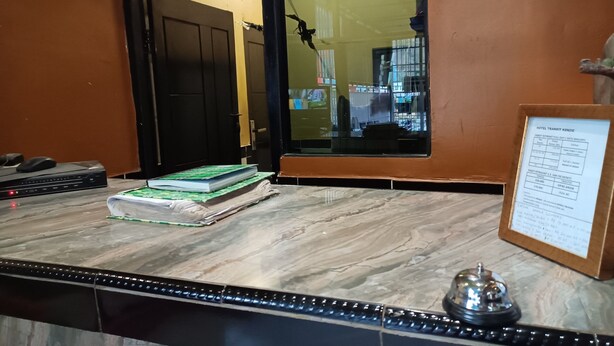 A hotel reception desk with a wooden counter, a bell, and a framed hotel transit information sign. - OYO 93485 Hotel Kenzie Sentani (Sentani)
