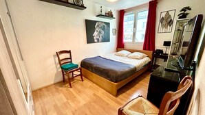 Un dormitorio con cama, escritorio, silla y ventana con cortinas.