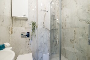 A bathroom with a glass shower enclosure, marble walls, and a white sink.