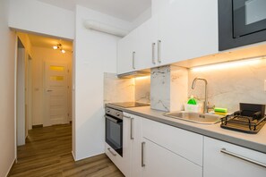 A compact kitchen with white cabinets, a stainless steel sink, and a built-in oven.