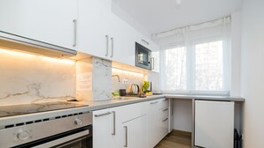 Een moderne keuken met witte kastjes, een ingebouwde oven, een magnetron en een kleine koelkast.