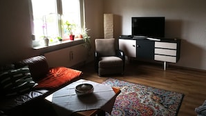 A living room with a sofa, a coffee table, a TV, a cabinet, and a window with plants.