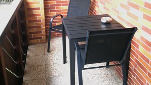 A corner patio with a metal table and chairs, a wall-mounted light fixture, and a small shelf.