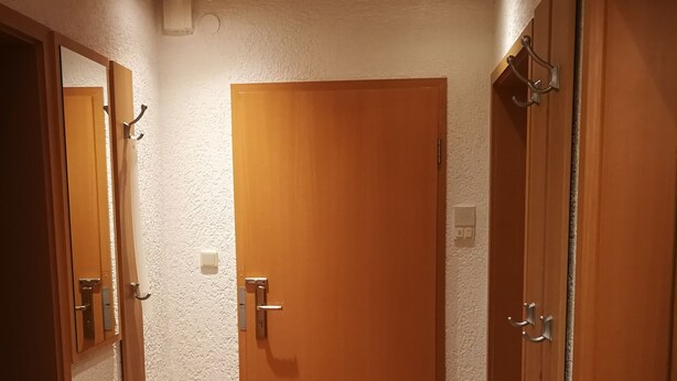 A hallway with a wooden door, a mirror, and a coat rack.
