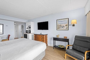Une chambre d’hôtel comprenant un lit, un bureau avec un téléviseur à écran plat, une chaise, une petite table et une lampe fixée au mur.