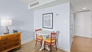 Un coin repas avec une table ronde, deux chaises, un buffet en bois, une lampe et un tableau encadré au mur.
