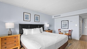 Une chambre d’hôtel avec un grand lit, des tables de chevet avec des lampes, un bureau avec des chaises et des tableaux encadrés au mur.