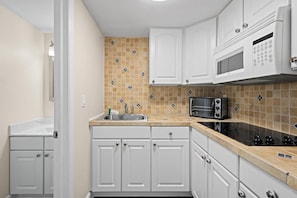A kitchen with white cabinets, a microwave, a stove, and a sink.