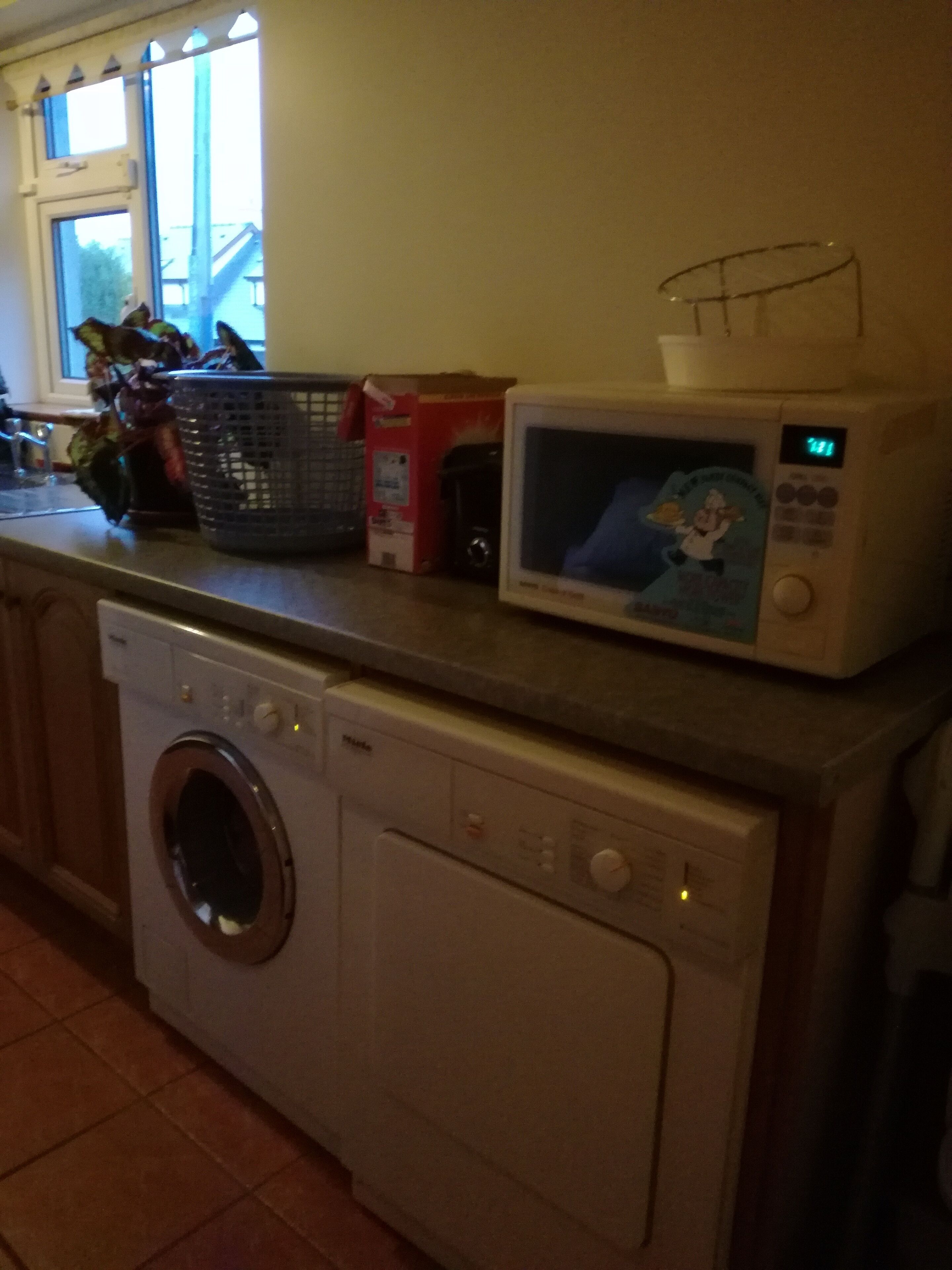 Une cuisine équipée d’un lave-linge, d’un four à micro-ondes et d’une fenêtre avec des rideaux.