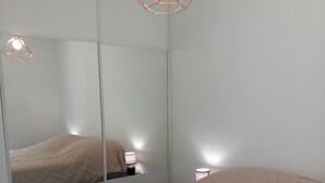 A bedroom with a large bed, a bedside table with a lamp, and a mirror reflecting the bed and lamp.