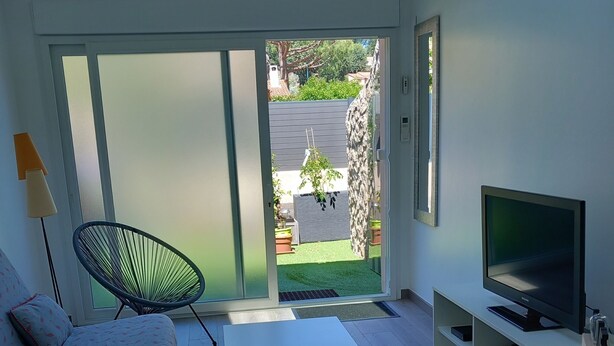A modern living room with a sofa, a coffee table, a TV on a stand, and a sliding glass door leading to a garden.