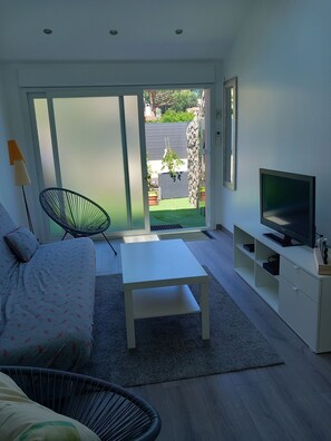 Un salon moderne avec un canapé, une table basse, un téléviseur posé sur un meuble et une porte-fenêtre coulissante donnant sur un jardin.