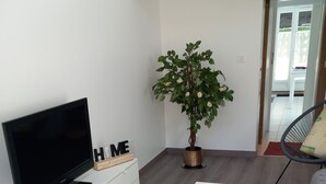 A modern living room with a flat-screen TV on a white cabinet, a potted plant, a white coffee table, and a door leading to an outdoor area.