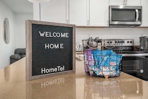 A kitchen counter with a welcome sign, a basket of snacks, and a microwave in the background.