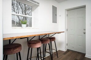 Una cocina con encimera blanca, una ventana con planta y una puerta blanca.