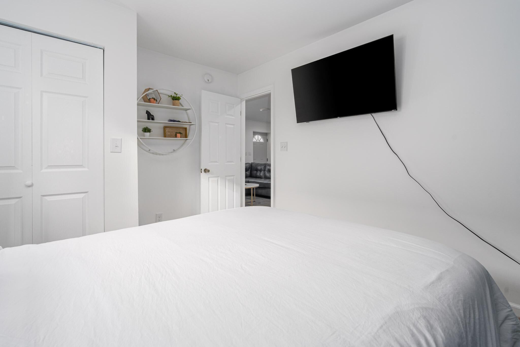 A bedroom with a bed, a TV mounted on the wall, a door, and a shelf with decorative items.