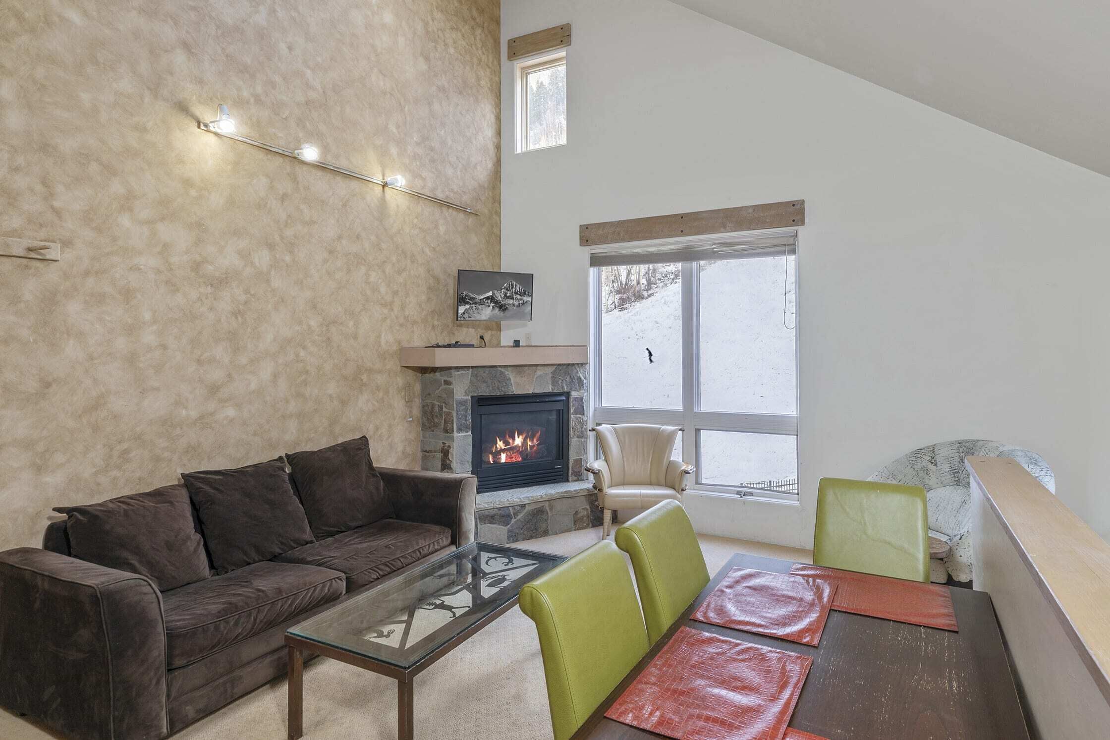 Un salon avec une cheminée en pierre, un canapé, une table basse en verre et une table à manger avec des chaises.