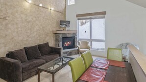 Un salon avec une cheminée en pierre, un canapé, une table basse en verre et une table à manger avec des chaises.