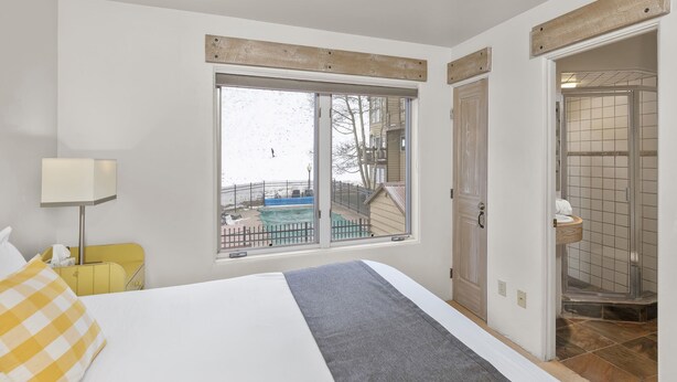 Une chambre à coucher comprenant un lit, une fenêtre, une table de chevet, une lampe et donnant sur une piscine extérieure.