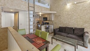 Un vaste espace de vie doté d’un haut plafond, une table à manger avec des chaises, un canapé et un coin cuisine équipé d’un four à micro-ondes et d’un évier.